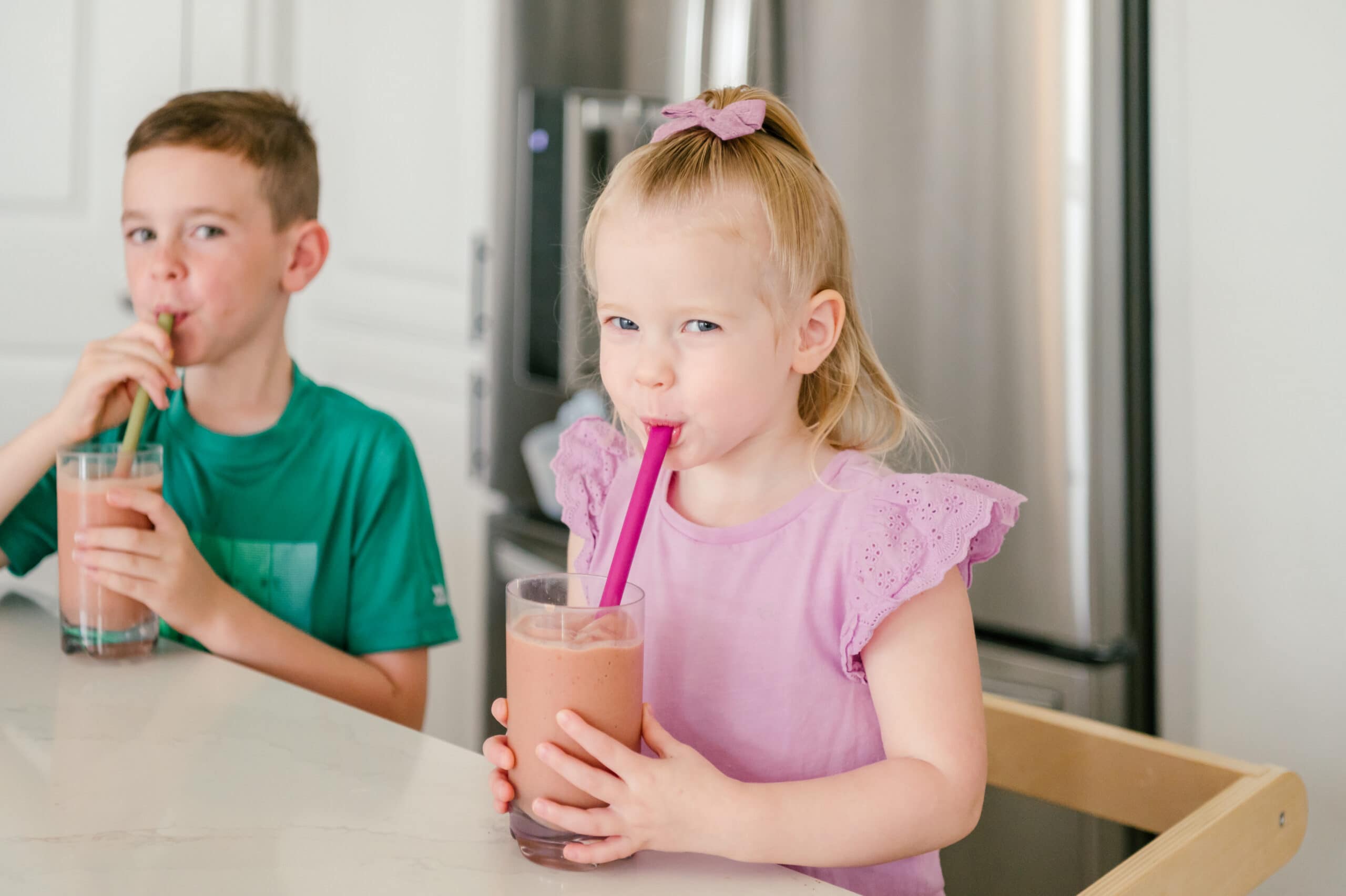 Two young kids in the kitchen drinking smoothies