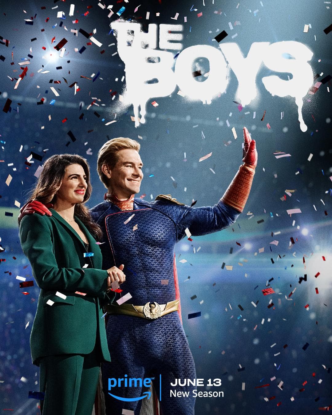 A man in a superhero costume and a woman in a green suit stand amidst a shower of confetti. The man waves while the woman holds his arm. The text reads 