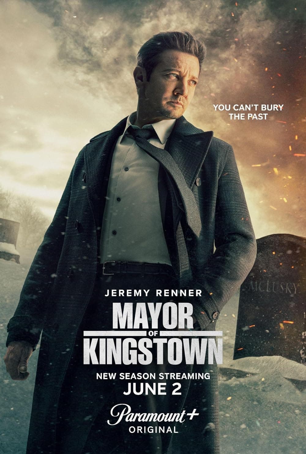 Poster for the TV series "Mayor of Kingstown," showing a man in a suit and overcoat standing in a snowy graveyard. The text reads: "You can't bury the past," "Jeremy Renner," "Mayor of Kingstown," "New season streaming June 2," and "Paramount+ Original." Wondering what to watch next? This is it.