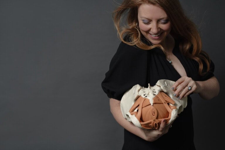 Dr. Krystal Lynn Couture looking down while holding a model pelvis
